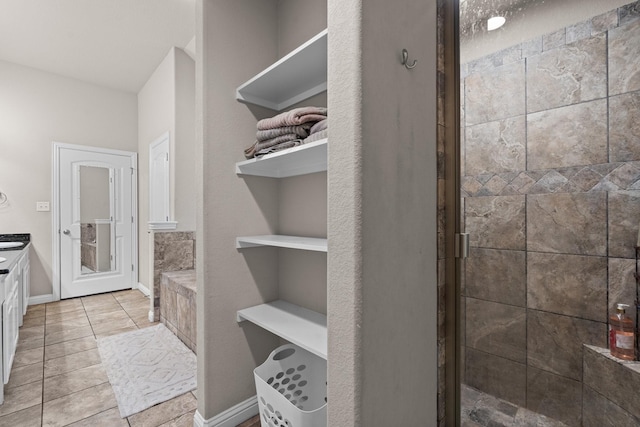 full bath featuring tiled shower, tile patterned flooring, vanity, and baseboards