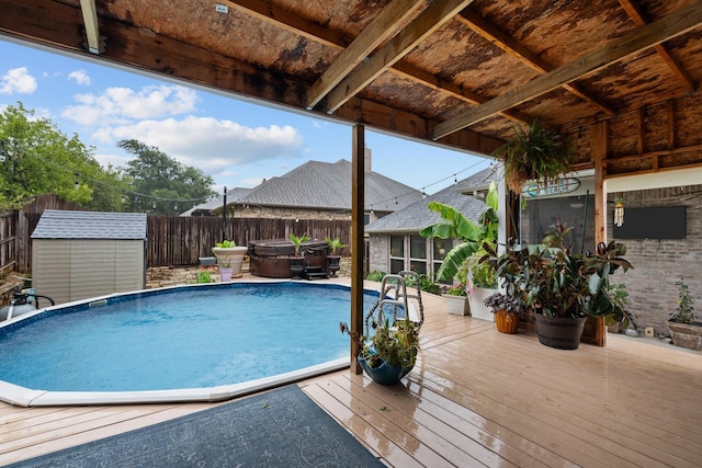 view of pool with a storage shed, a hot tub, a fenced backyard, an outbuilding, and a wooden deck