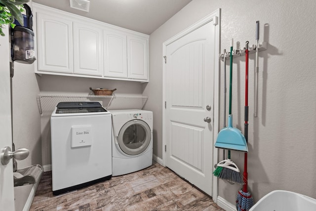 laundry room featuring washing machine and dryer, visible vents, baseboards, cabinet space, and light wood finished floors