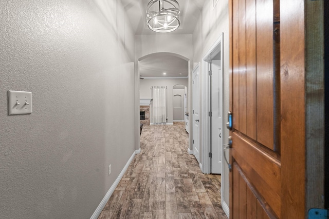 corridor featuring baseboards, arched walkways, dark wood-style flooring, and a textured wall