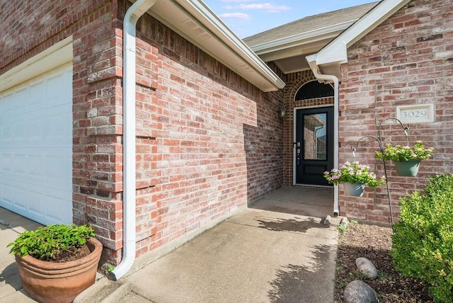 entrance to property featuring a garage and brick siding
