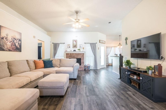 living room featuring dark wood-style flooring, ceiling fan, and a brick fireplace