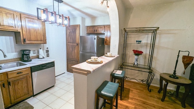 kitchen with a breakfast bar area, appliances with stainless steel finishes, sink, light hardwood / wood-style floors, and decorative light fixtures