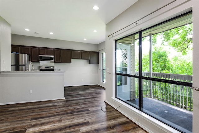 kitchen with dark brown cabinets, stainless steel appliances, light stone counters, and dark hardwood / wood-style floors