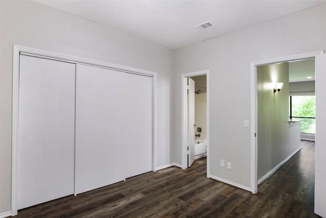 unfurnished bedroom with ensuite bathroom, dark hardwood / wood-style flooring, and a closet