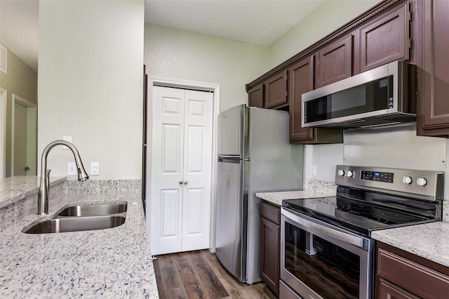 kitchen with sink, light stone countertops, appliances with stainless steel finishes, dark brown cabinets, and dark hardwood / wood-style flooring