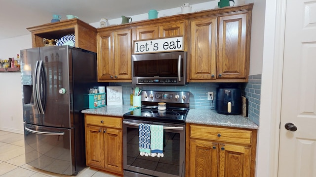 kitchen featuring appliances with stainless steel finishes, light stone countertops, backsplash, and light tile patterned floors