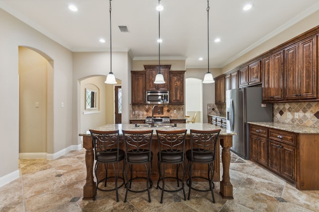 kitchen with light tile patterned floors, backsplash, appliances with stainless steel finishes, pendant lighting, and a center island with sink