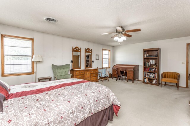 bedroom featuring multiple windows, light carpet, ceiling fan, and a textured ceiling