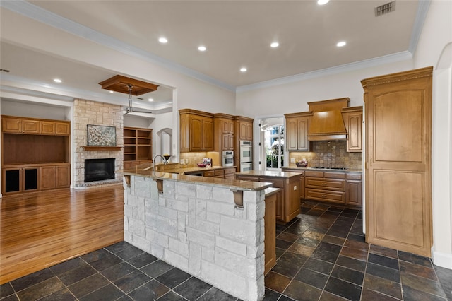 kitchen with dark hardwood / wood-style flooring, ornamental molding, a breakfast bar, custom range hood, and a large island with sink