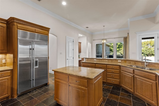 kitchen featuring pendant lighting, built in fridge, sink, ornamental molding, and tasteful backsplash