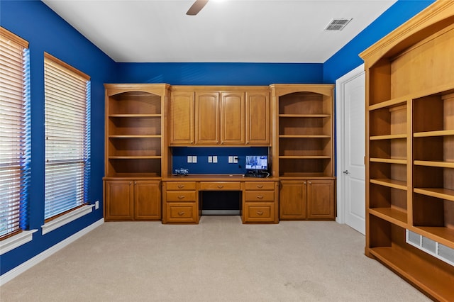 unfurnished office featuring light carpet, built in desk, and ceiling fan