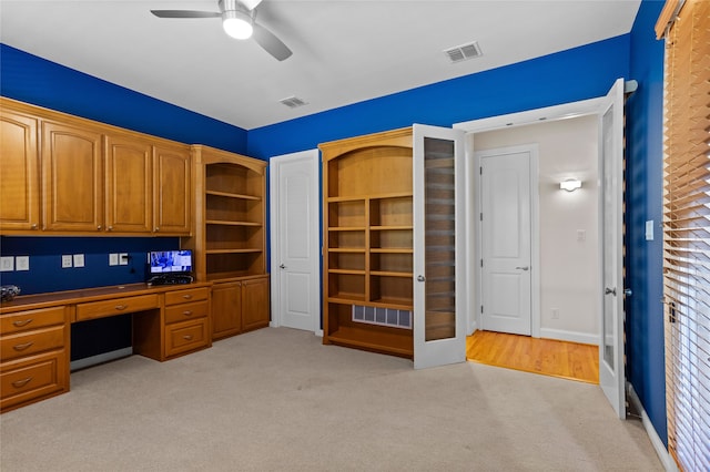 unfurnished office featuring light carpet, ceiling fan, and built in desk