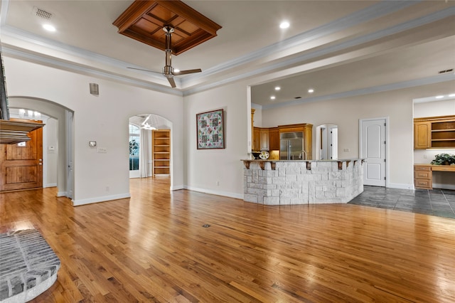 unfurnished living room with a tray ceiling, ceiling fan, dark wood-type flooring, and ornamental molding