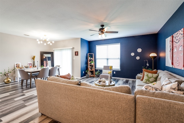 living room with ceiling fan with notable chandelier, light hardwood / wood-style flooring, and a textured ceiling