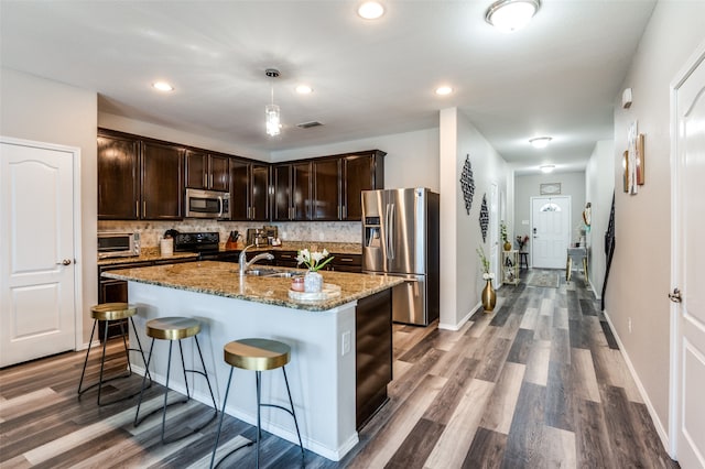 kitchen with tasteful backsplash, stainless steel appliances, dark brown cabinets, stone countertops, and hardwood / wood-style flooring