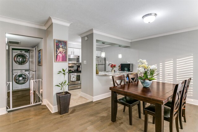 dining space featuring stacked washing maching and dryer, hardwood / wood-style flooring, and crown molding