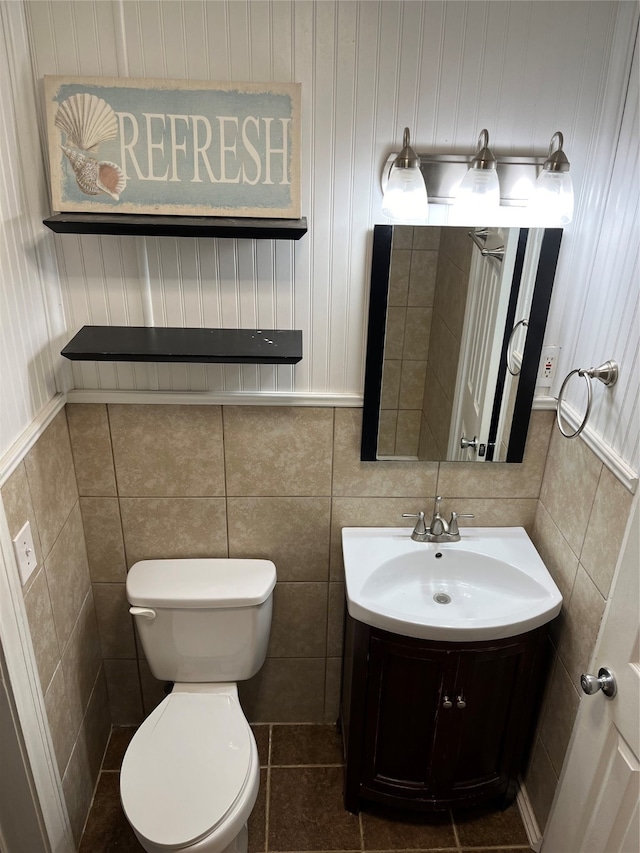 bathroom featuring tile patterned floors, toilet, tile walls, wooden walls, and vanity