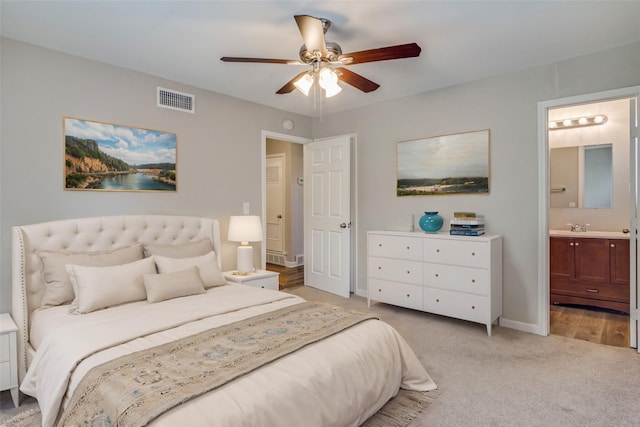 bedroom featuring visible vents, ensuite bathroom, a ceiling fan, light carpet, and a sink