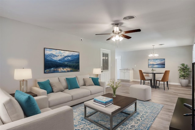 living area with ceiling fan with notable chandelier, light wood-style flooring, visible vents, and baseboards