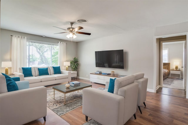 living room featuring a ceiling fan, visible vents, baseboards, and wood finished floors