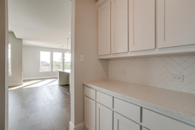 interior space with light stone countertops, hardwood / wood-style floors, decorative backsplash, and white cabinets