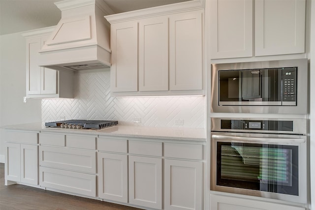 kitchen with light stone countertops, white cabinetry, stainless steel appliances, custom range hood, and dark hardwood / wood-style floors