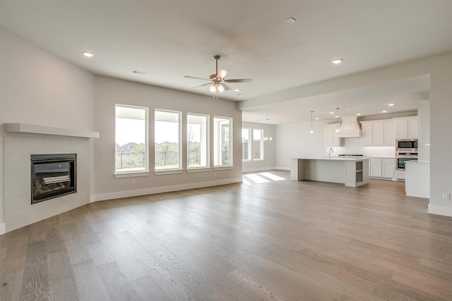 unfurnished living room with a tiled fireplace, light hardwood / wood-style floors, sink, and ceiling fan