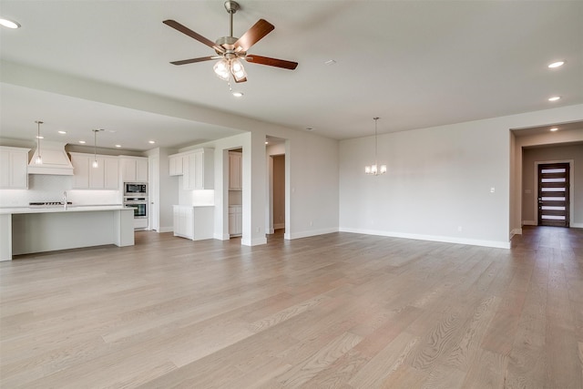 unfurnished living room with sink, ceiling fan with notable chandelier, and light wood-type flooring