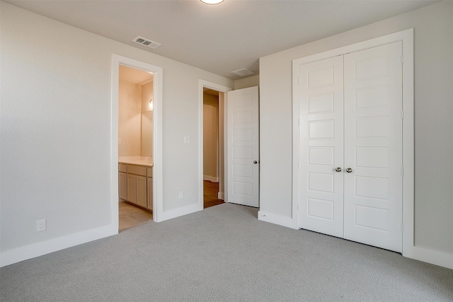 unfurnished bedroom featuring a closet, light carpet, and ensuite bath