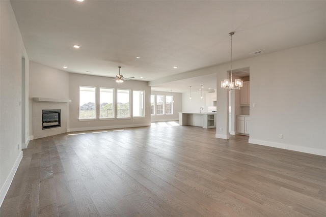 unfurnished living room with sink, hardwood / wood-style flooring, and ceiling fan with notable chandelier