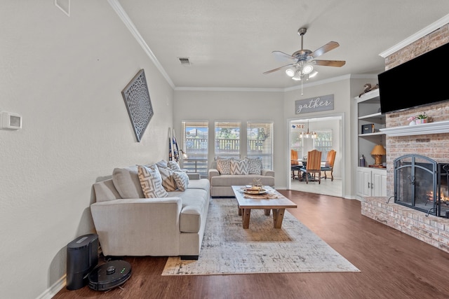 living room with hardwood / wood-style floors, ceiling fan, crown molding, a fireplace, and built in shelves