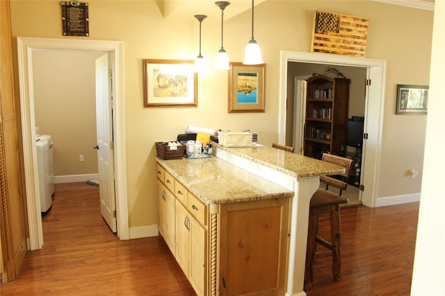 kitchen featuring a kitchen breakfast bar, wood-type flooring, light stone counters, washer and clothes dryer, and pendant lighting