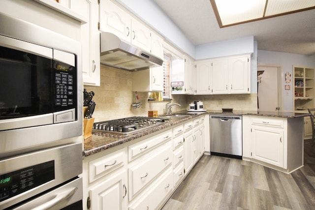 kitchen with hardwood / wood-style flooring, appliances with stainless steel finishes, decorative backsplash, and dark stone counters