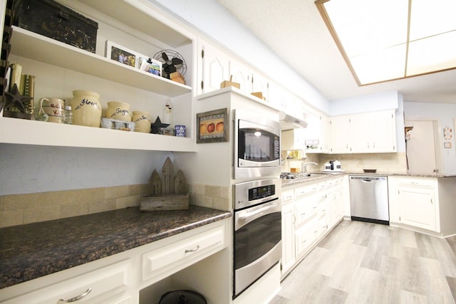 kitchen with white cabinetry, stainless steel appliances, light hardwood / wood-style floors, and dark stone countertops