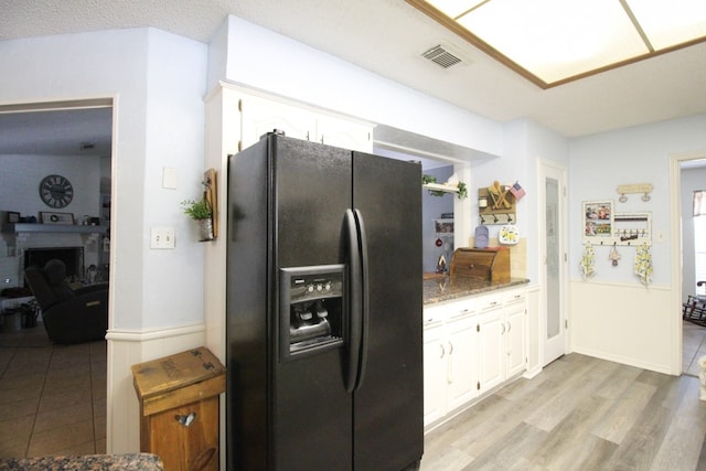 kitchen featuring white cabinets, light wood-type flooring, light stone counters, and black fridge with ice dispenser