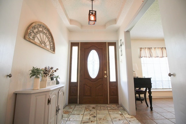 tiled entrance foyer with a textured ceiling and a raised ceiling