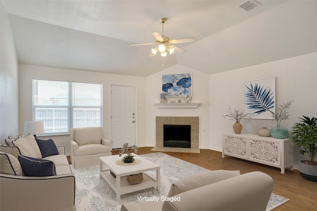 living area with vaulted ceiling, visible vents, a tile fireplace, and wood finished floors