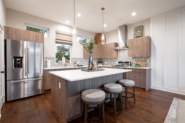 kitchen featuring wall chimney range hood, dark hardwood / wood-style floors, a kitchen island, appliances with stainless steel finishes, and backsplash