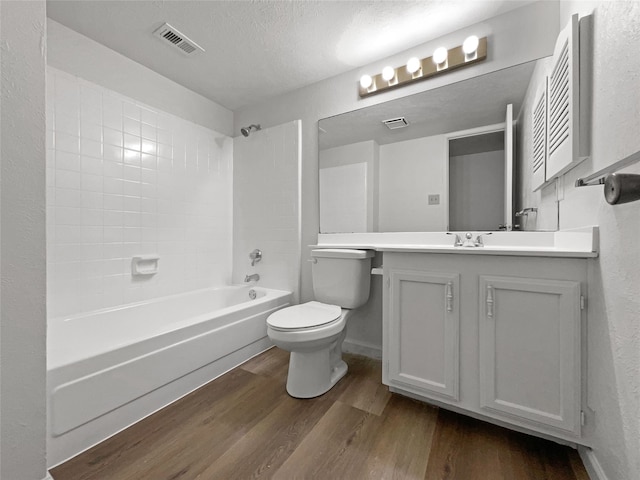 full bathroom with vanity, hardwood / wood-style flooring, tiled shower / bath combo, toilet, and a textured ceiling