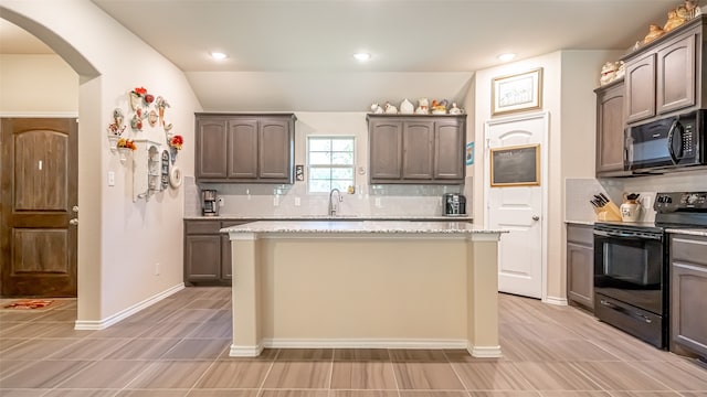 kitchen featuring black appliances, light stone counters, a center island, and dark brown cabinets