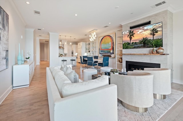 living room with crown molding, a large fireplace, an inviting chandelier, and light wood-type flooring