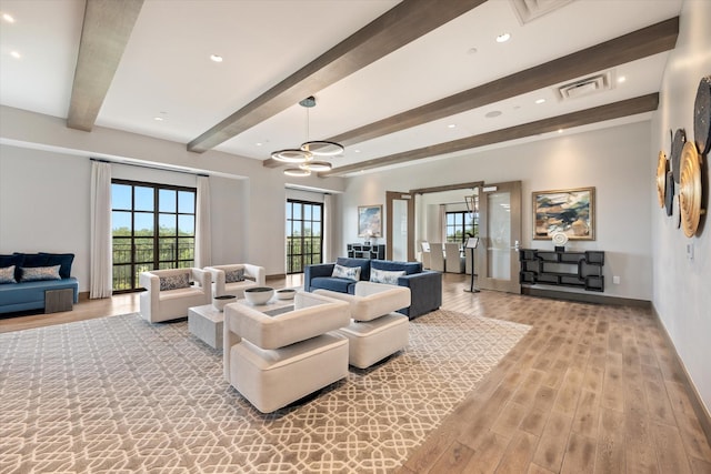 living room featuring beamed ceiling, wood-type flooring, plenty of natural light, and an inviting chandelier