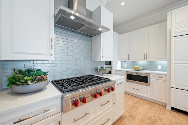 kitchen featuring white cabinetry, stainless steel appliances, and wall chimney range hood