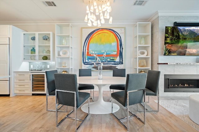 dining space featuring an inviting chandelier, light wood-type flooring, ornamental molding, a tile fireplace, and beverage cooler