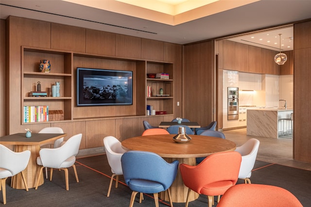 carpeted dining area featuring built in features, wood walls, and sink