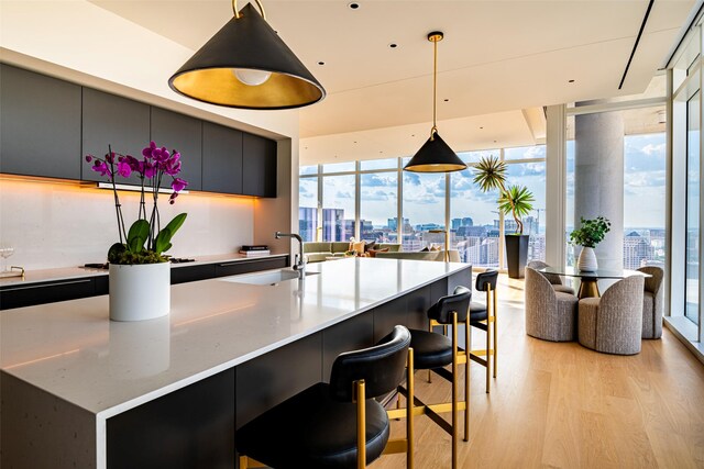 kitchen with hanging light fixtures, light hardwood / wood-style flooring, a wall of windows, sink, and an island with sink