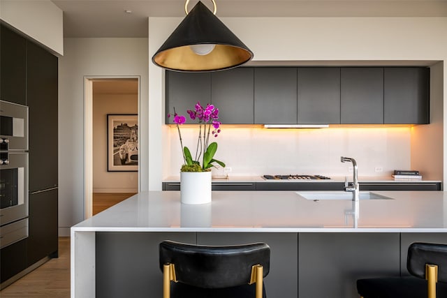 kitchen with a center island with sink, light hardwood / wood-style floors, a breakfast bar, sink, and stainless steel oven