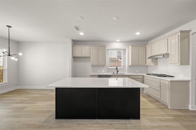 kitchen with pendant lighting, sink, a center island, a notable chandelier, and light wood-type flooring