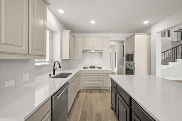 kitchen with light stone counters, sink, tasteful backsplash, light hardwood / wood-style flooring, and stainless steel appliances